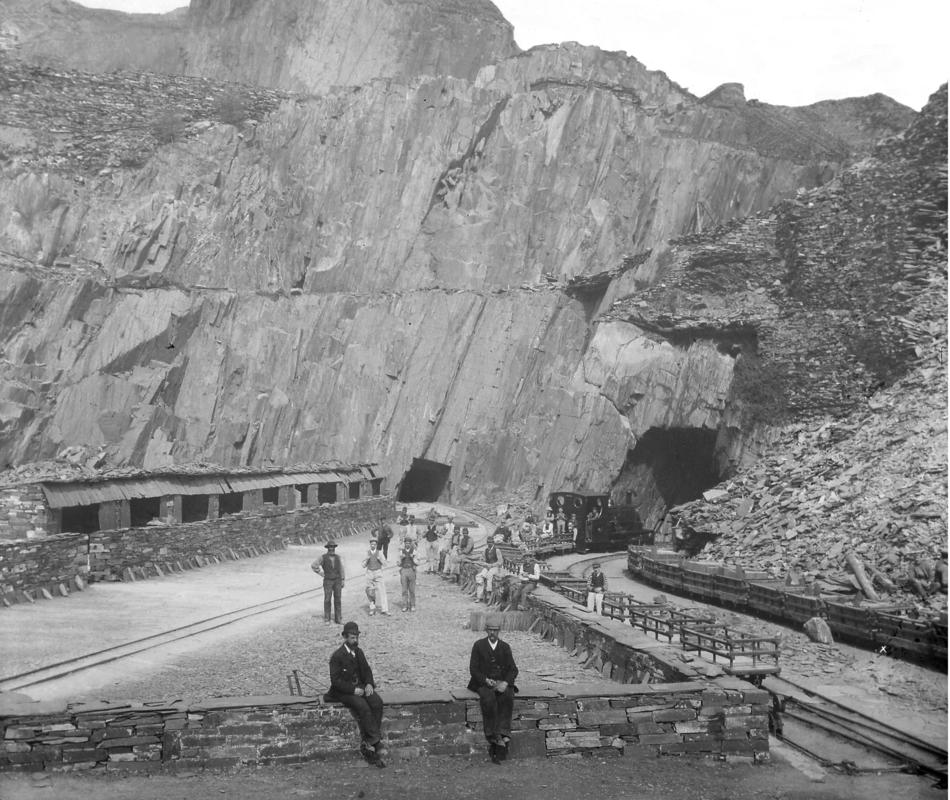 View of one of the 'ponciau' (galleries) at Dinorwic Quarry, showing quarrymen, gwaliau, and  a steam locomotive hauling slate loader wagons