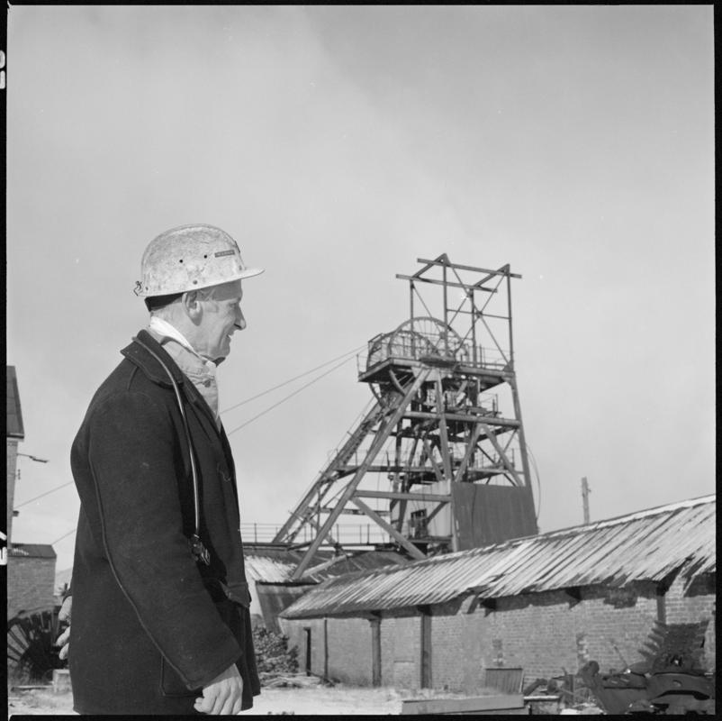 Black and white film negative showing Glyn Morgan, NCB Manager with the headgear in the background, Big Pit Colliery.