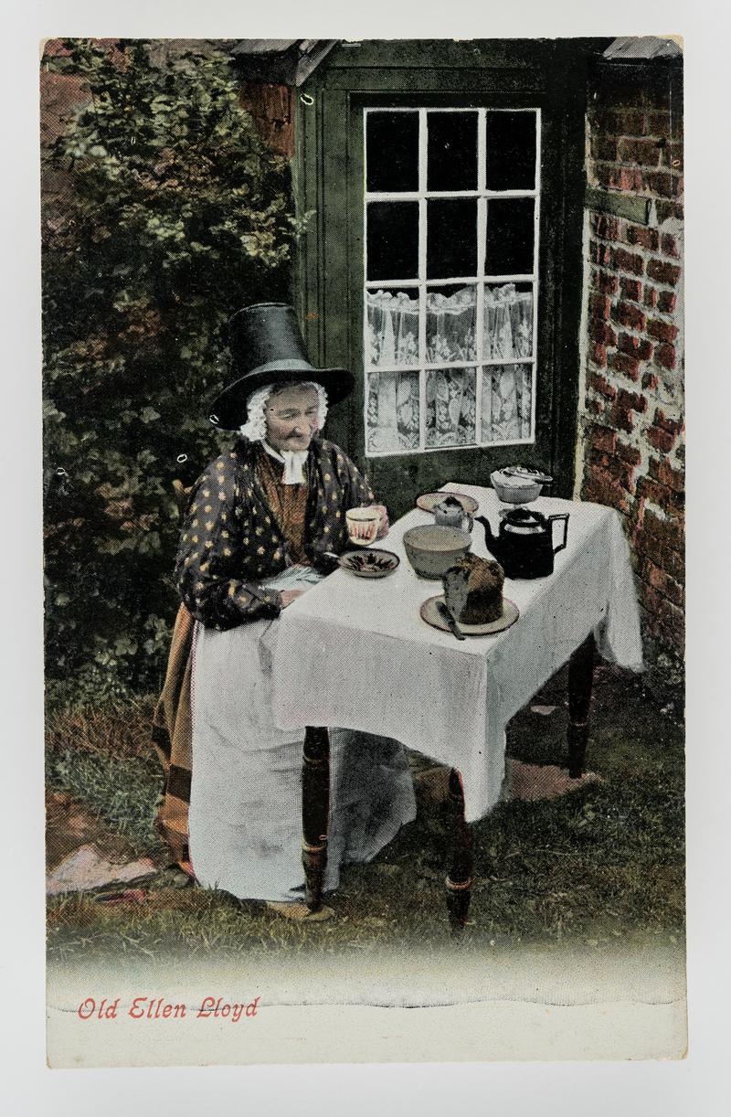 Old Ellen Lloyd, Bettws-y-coed, seated at tea table outside her house, wearing Welsh costume.