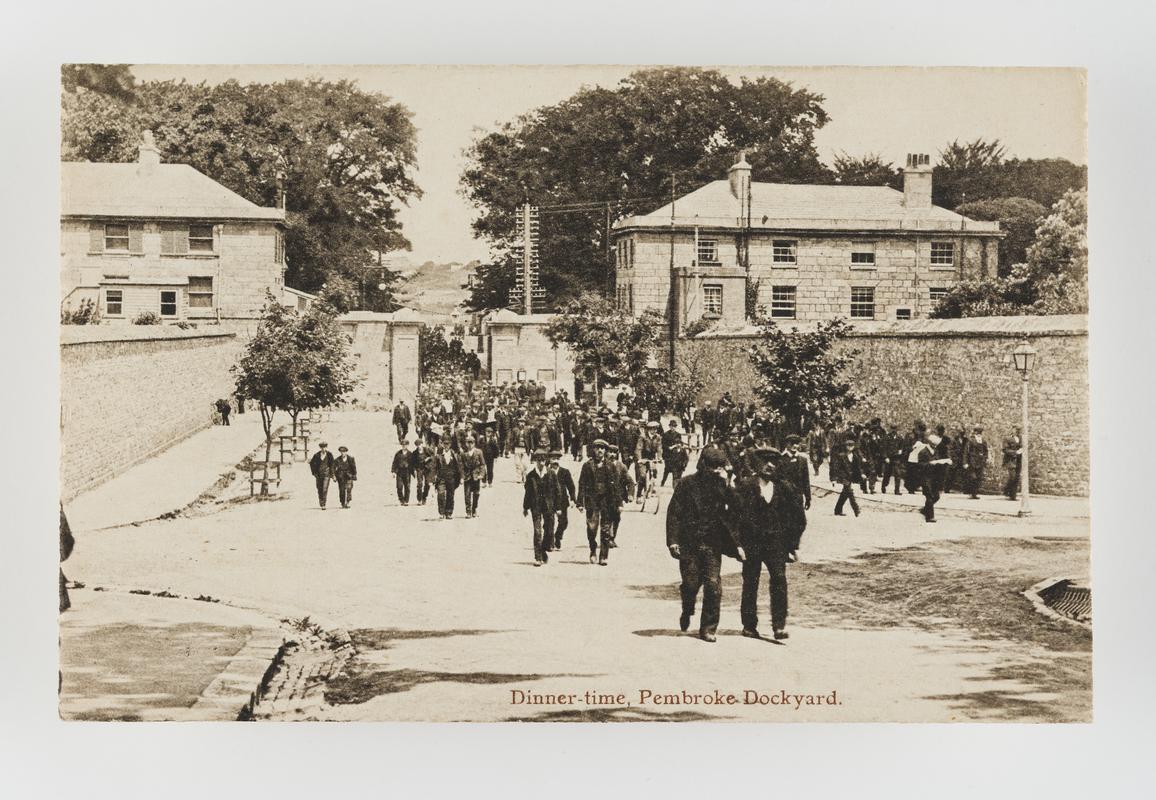 Dinner-time at dockyard, Pembroke Dock, showing large group of men walking up the road.