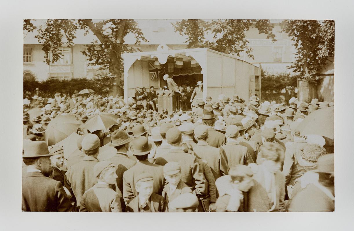 Outdoor photograph of a crowd of people listenning to a speech.