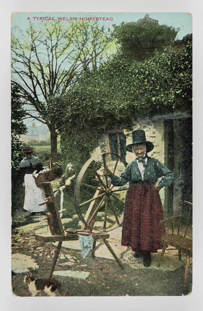 Ellen Lloyd, Bettws-y-coed in Welsh dress standing by spinning wheel outside cottage.  Title:  'A Typical Welsh homestead'.