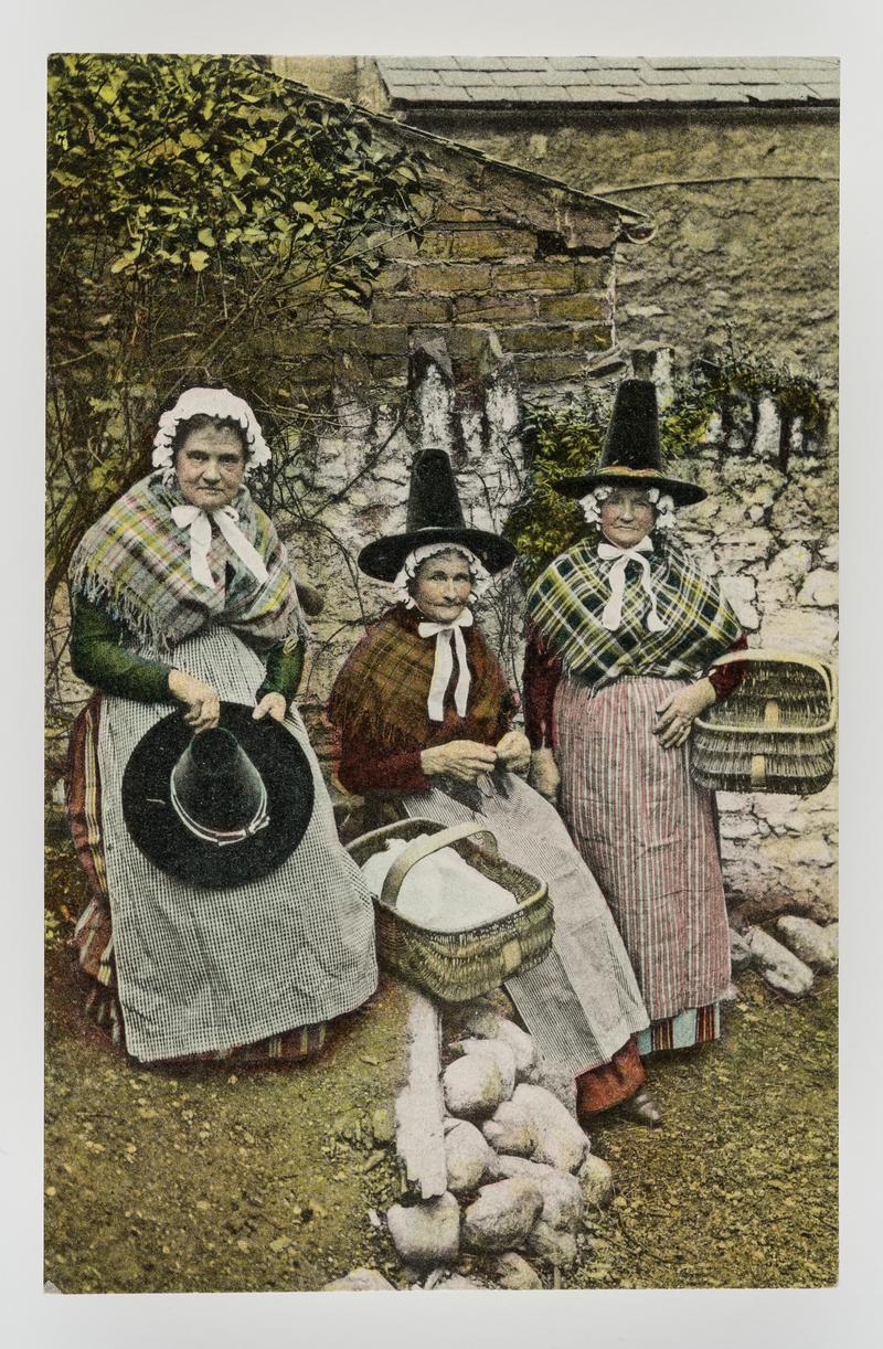 3 women in Welsh costume, 2 with large baskets the other holding her black hat.