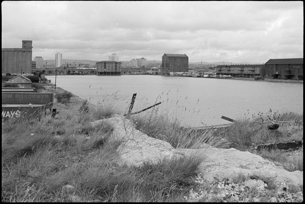 View from Bute East Dock looking North. The tall buildings of the city are visible beyond the old warehouses.
