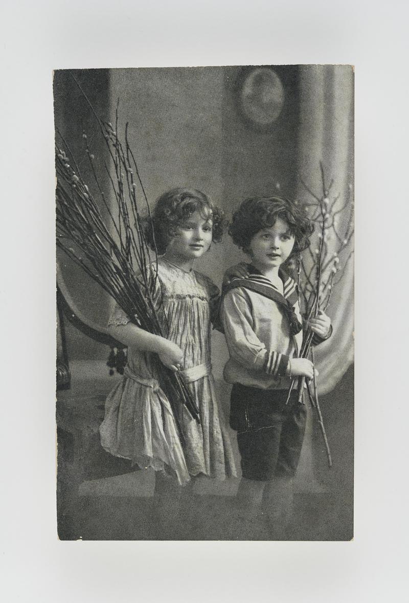 Studio photograph of a young girl and boy - holding twigs. Boy wearing sailor suit.