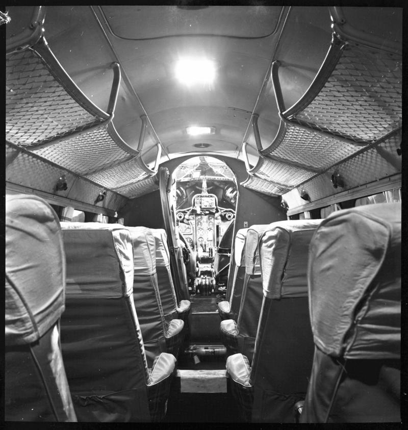 Looking forward along the passenger cabin of a De Havilland Dove aircraft through the open door to the cockpit.