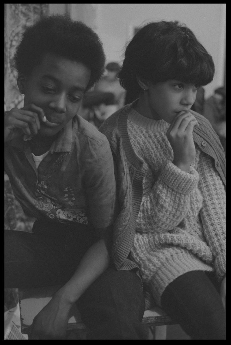 Two girls sat at side of hall in Butetown Youth Club.