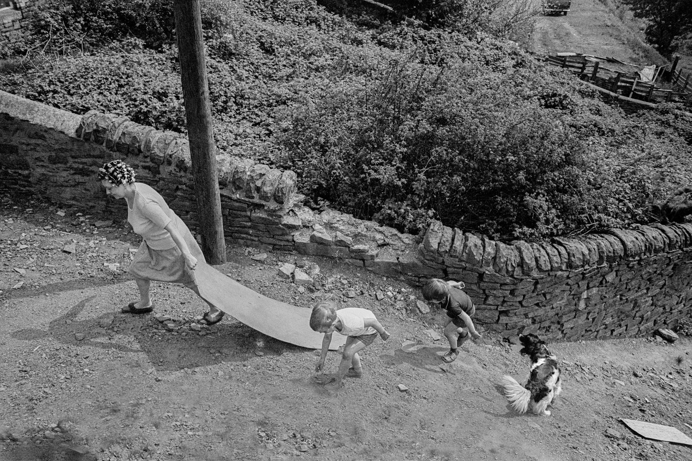 Family climbing to the top of a slag heap with a piece of board to use it as a slide. Abertillery, Wales