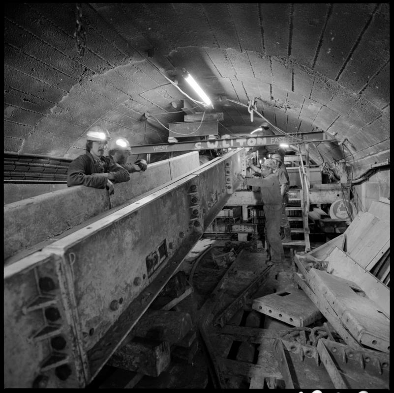 Black and white film negative showing fitters at work in the reconstructed pit bottom, prior to the fitting of the skips, Lady Windsor Colliery.