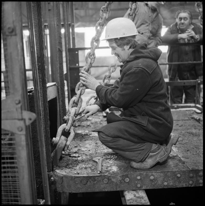 Black and white film negative showing man carrying out maintenance work on top of cage at pit top, Big Pit Colliery January 1982.  'Big Pit Blaenavon Jan 1982' is transcribed from original negative bag.