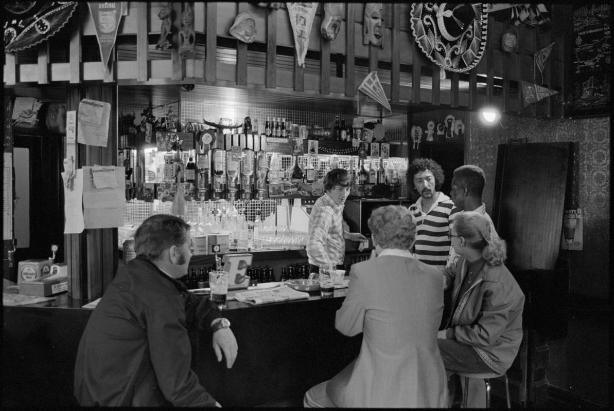Interior view of the Ship & Pilot public house showing people drinking at the bar, Mount Stuart Square, Butetown.