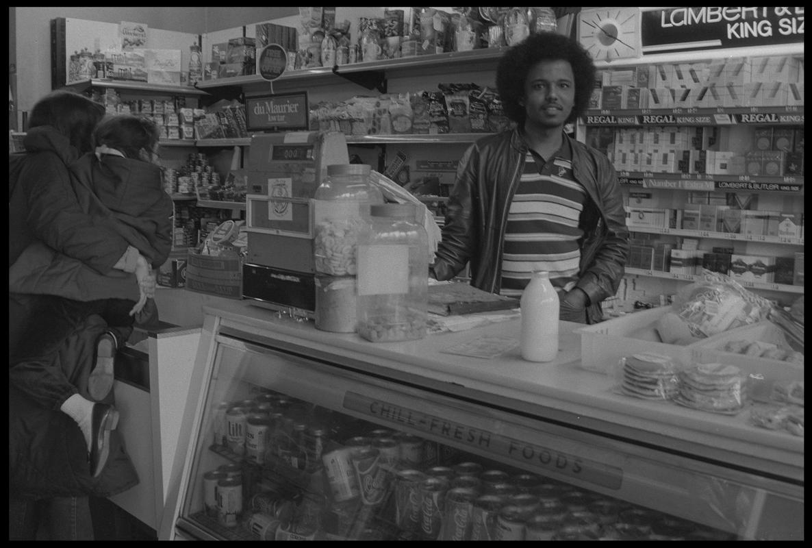 Woman carrying child, standing at counter in supermarket, Loudoun Square, Butetown.