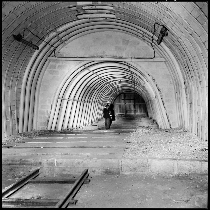 Black and white film negative showing a man standing in a cleared roadway, underground at Merthyr Vale Colliery.