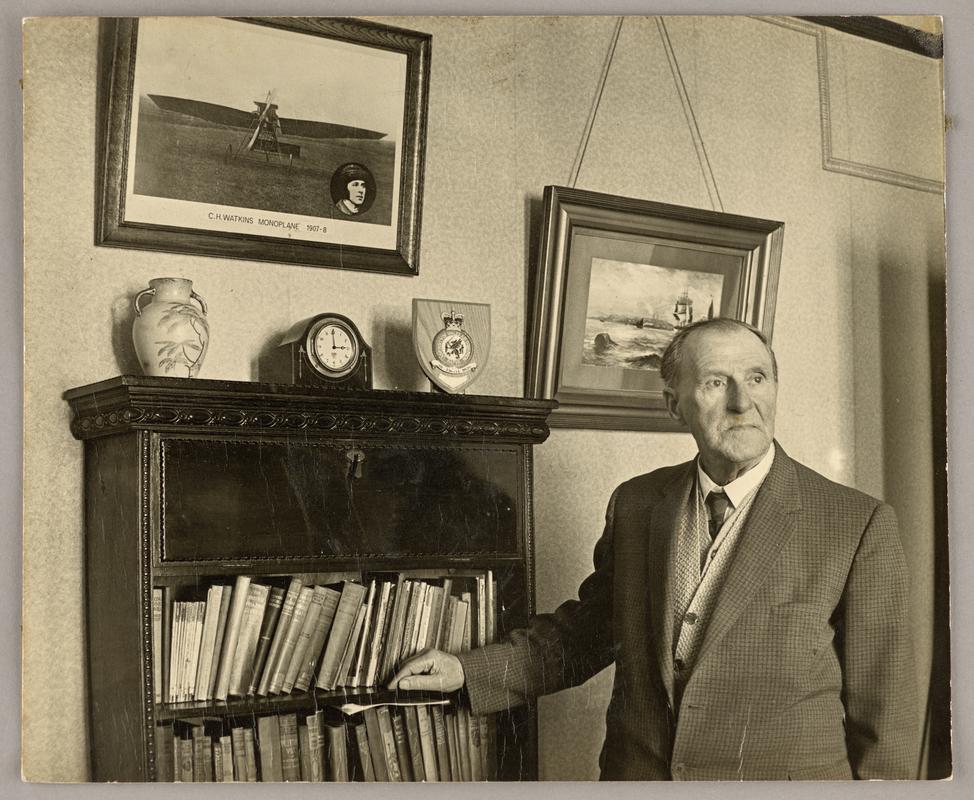 View of C.H. Watkins standing infront of bookcase at home.