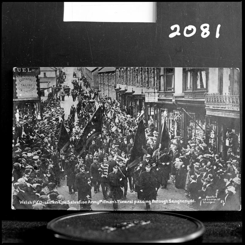 Black and white film negative of a photograph showing a funeral procession passing through Senghenydd.  Caption on photograph reads 'Welsh Pit Disaster. The Salvation Army Pitman's funeral passing through Senghenydd'.
