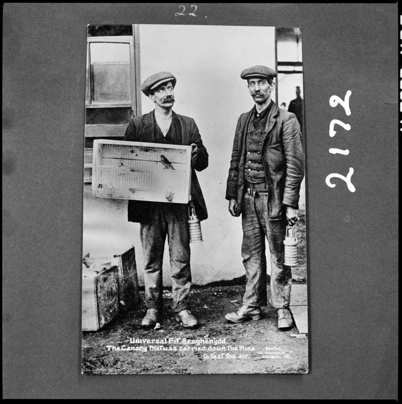 Black and white film negative of a photograph showing two men, one of whom is carrying a canary in a cage, Universal Colliery, 1913.  'Sen 1913' is transcribed from original negative bag.