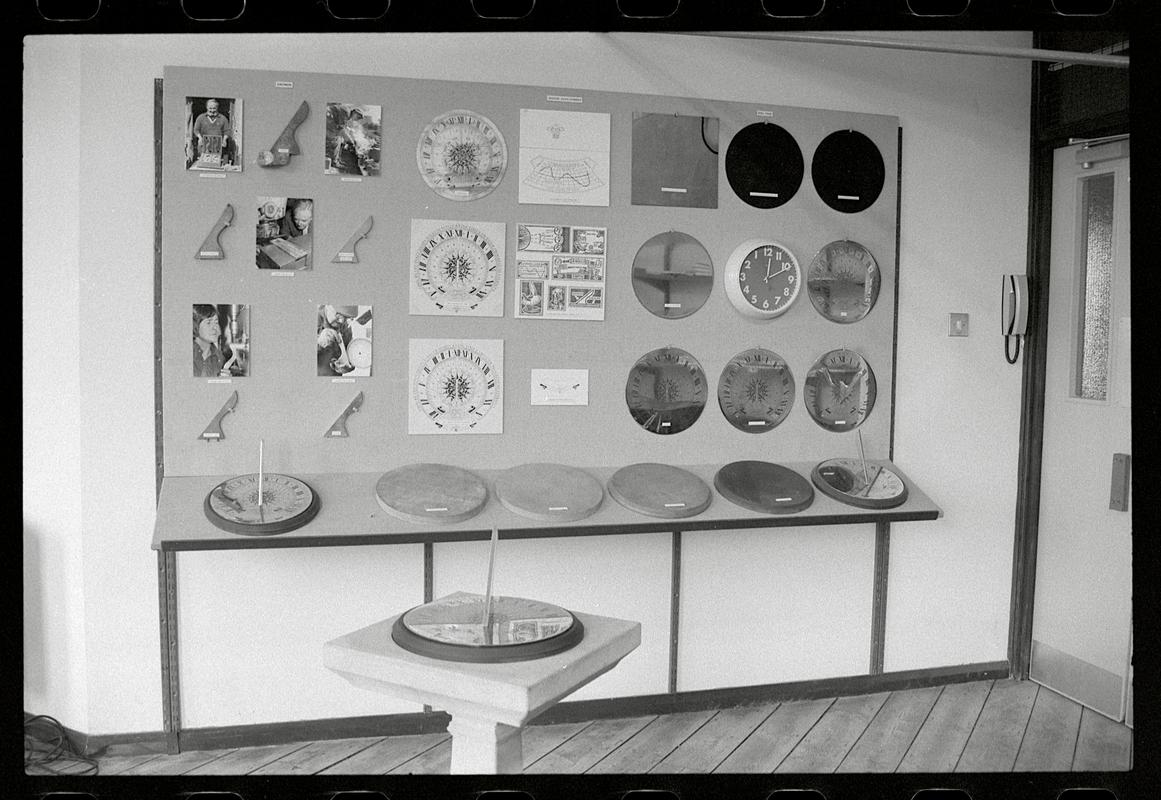 Display of sundials on wall, and an upright sundial in foreground of workshop.