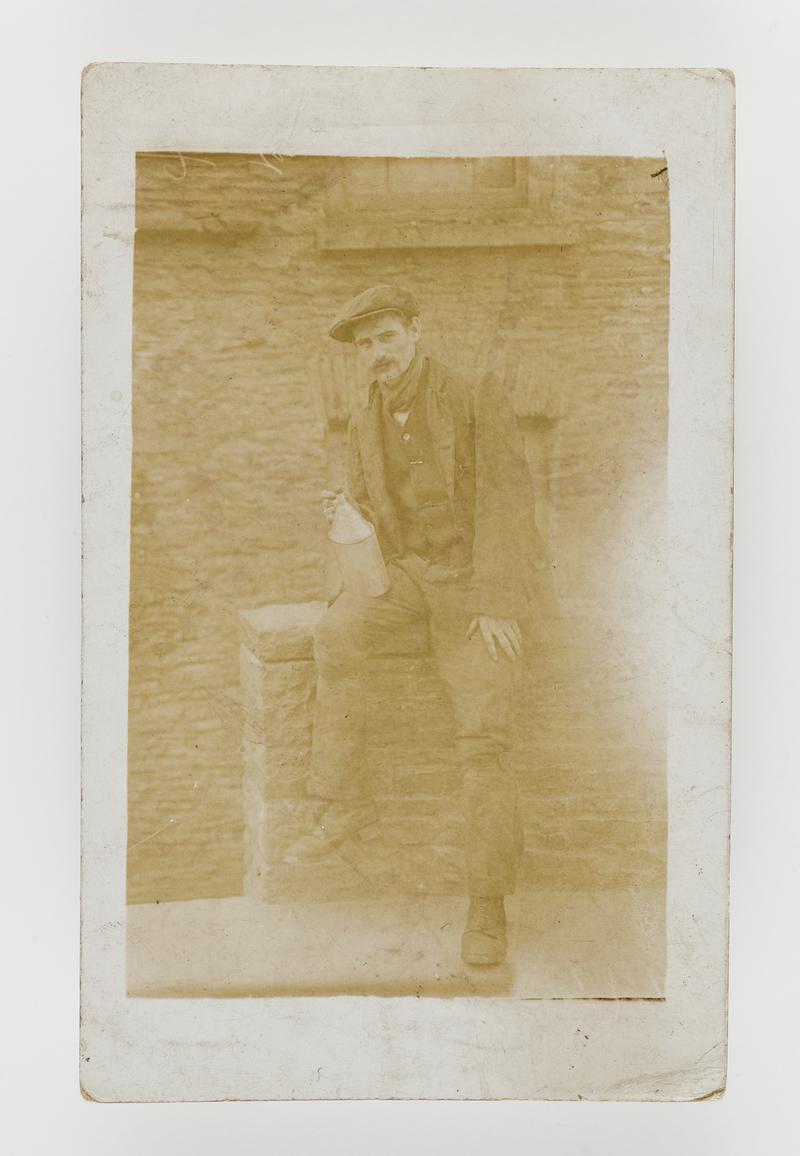 Photograph of a miner sitting on a wall holding a bottle.  Taken at Ty'n y Cae Road, Penygraig, Glam.  He worked at Ely Colliery