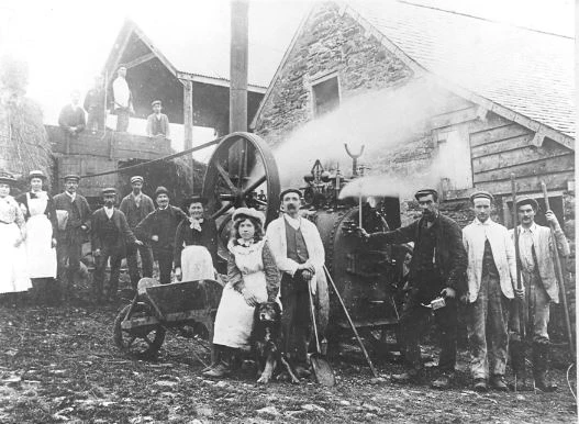 Oedolion a phlant yn sefyll o amgylch peiriant dyrnu ar fferm Tai'n y Cwm, Cefnddwysarn.