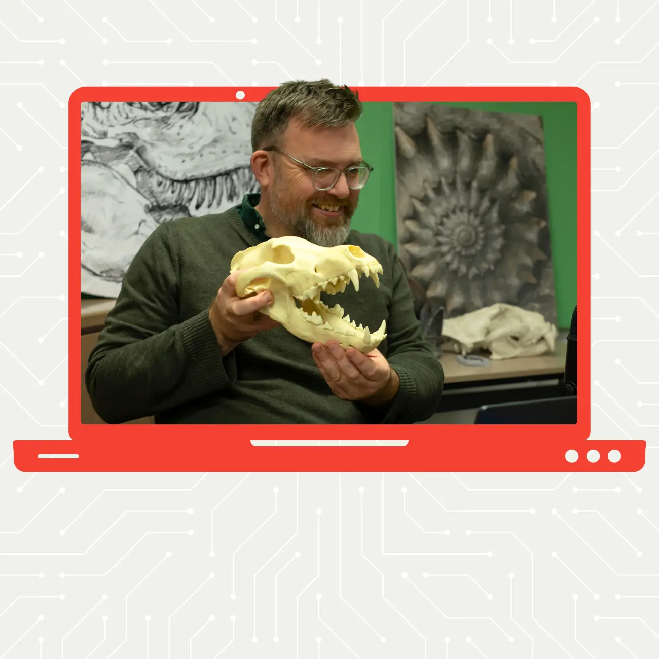 Dyn mewn sbectol yn dal penglog deinosor i fyny at gamera