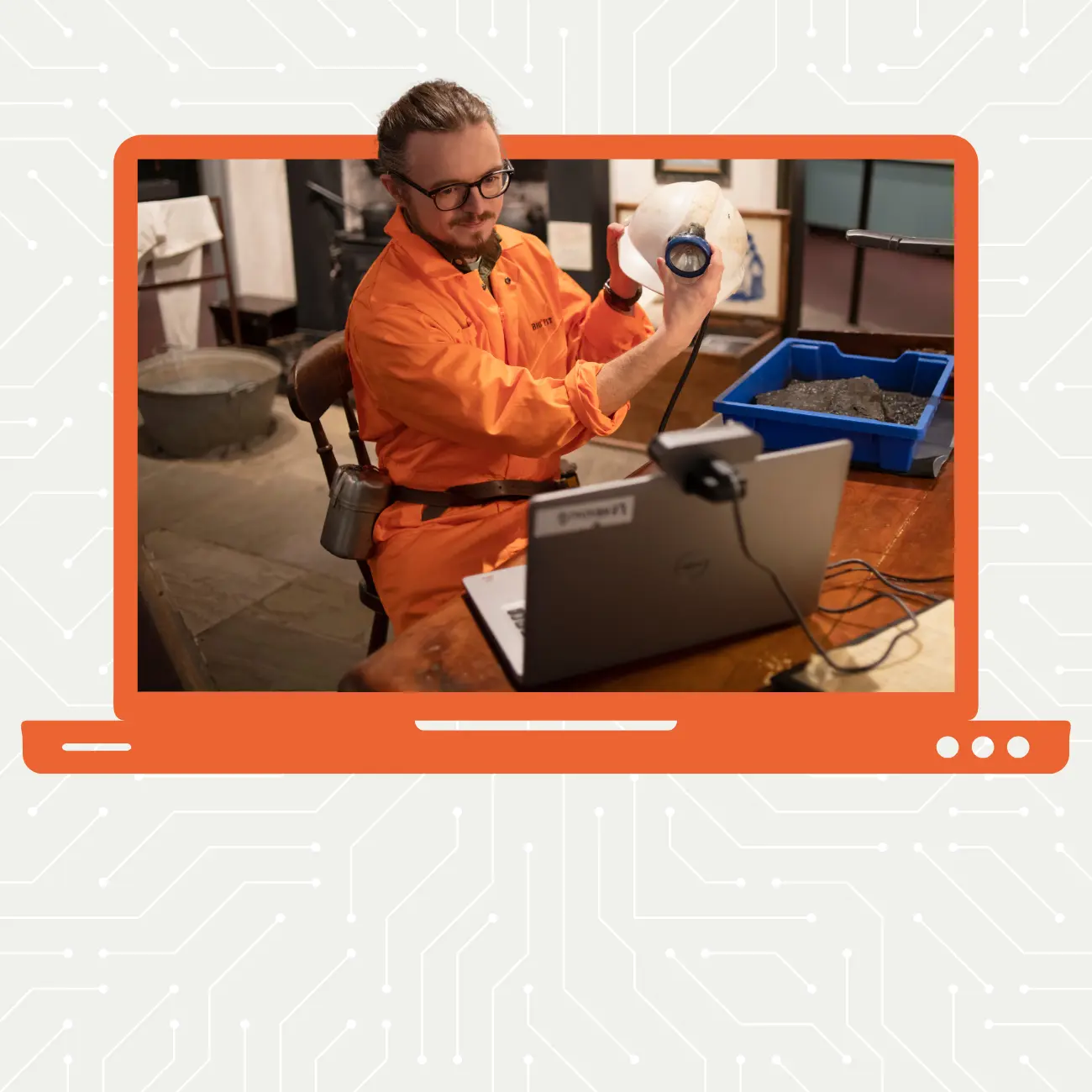 Dyn mewn siwt neidio oren yn dal helmed gyda fflachlamp pen i fyny at gamera