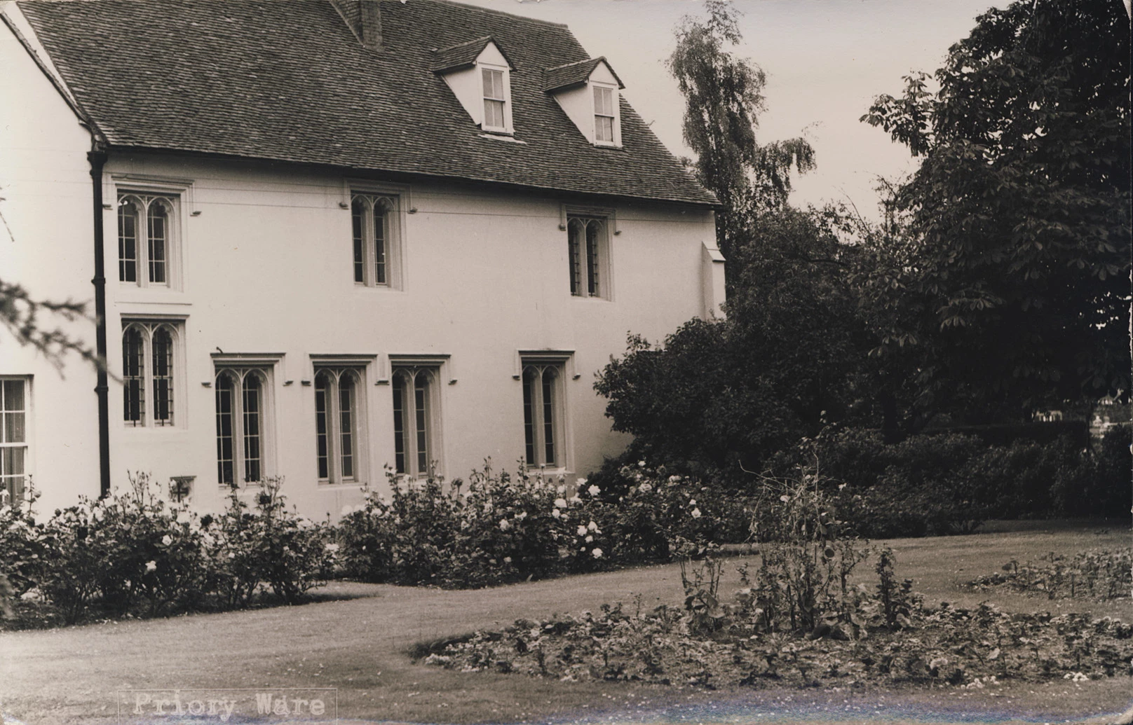 Ffotograff sepia o dŷ gyda waliau gwyn wedi'u plastro, ffenestri Gothig a gardd fawr.