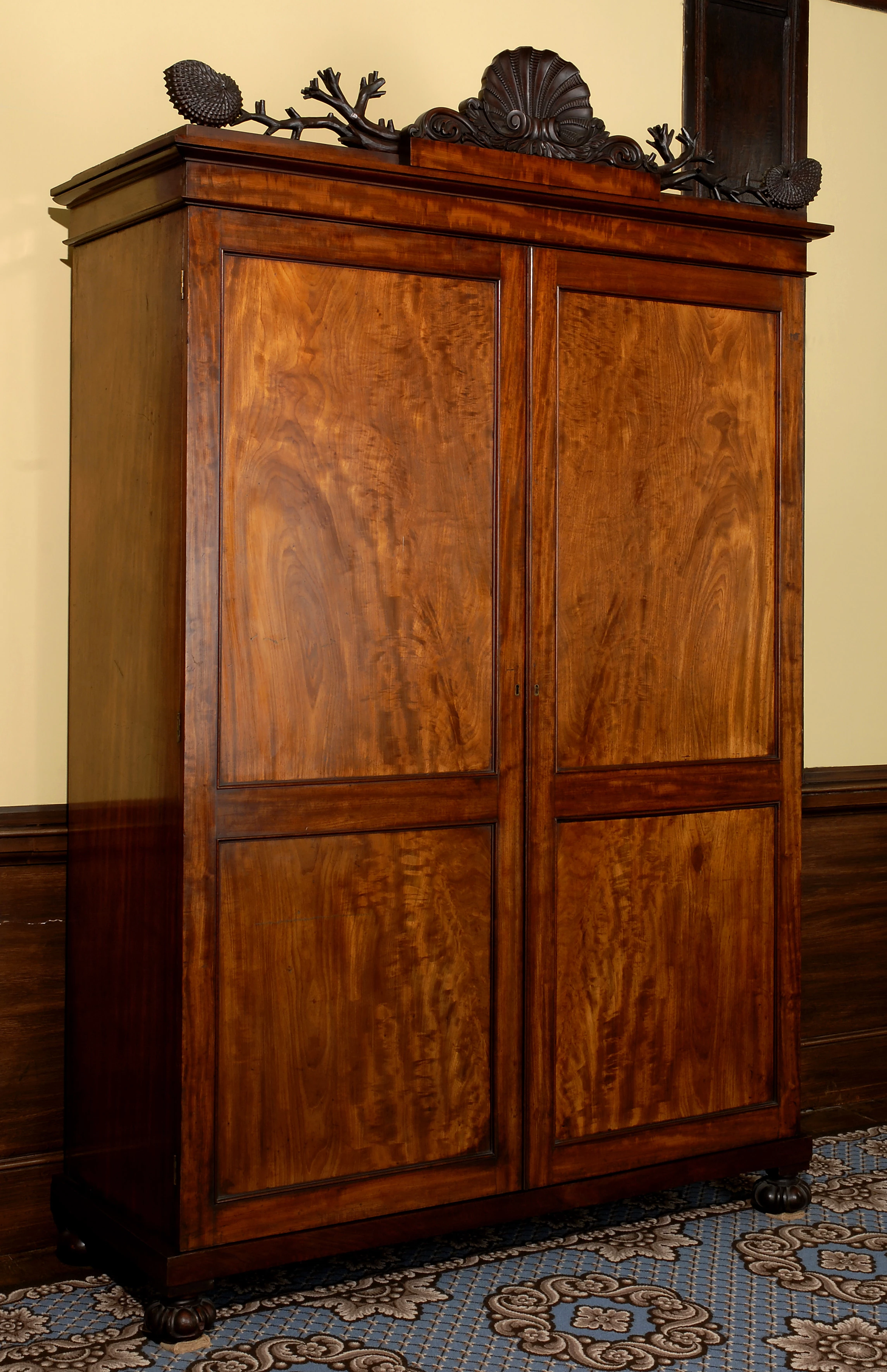 Cabinet mahogani gyda dau ddrws mawr a cherfiadau o gregyn ar y brig.