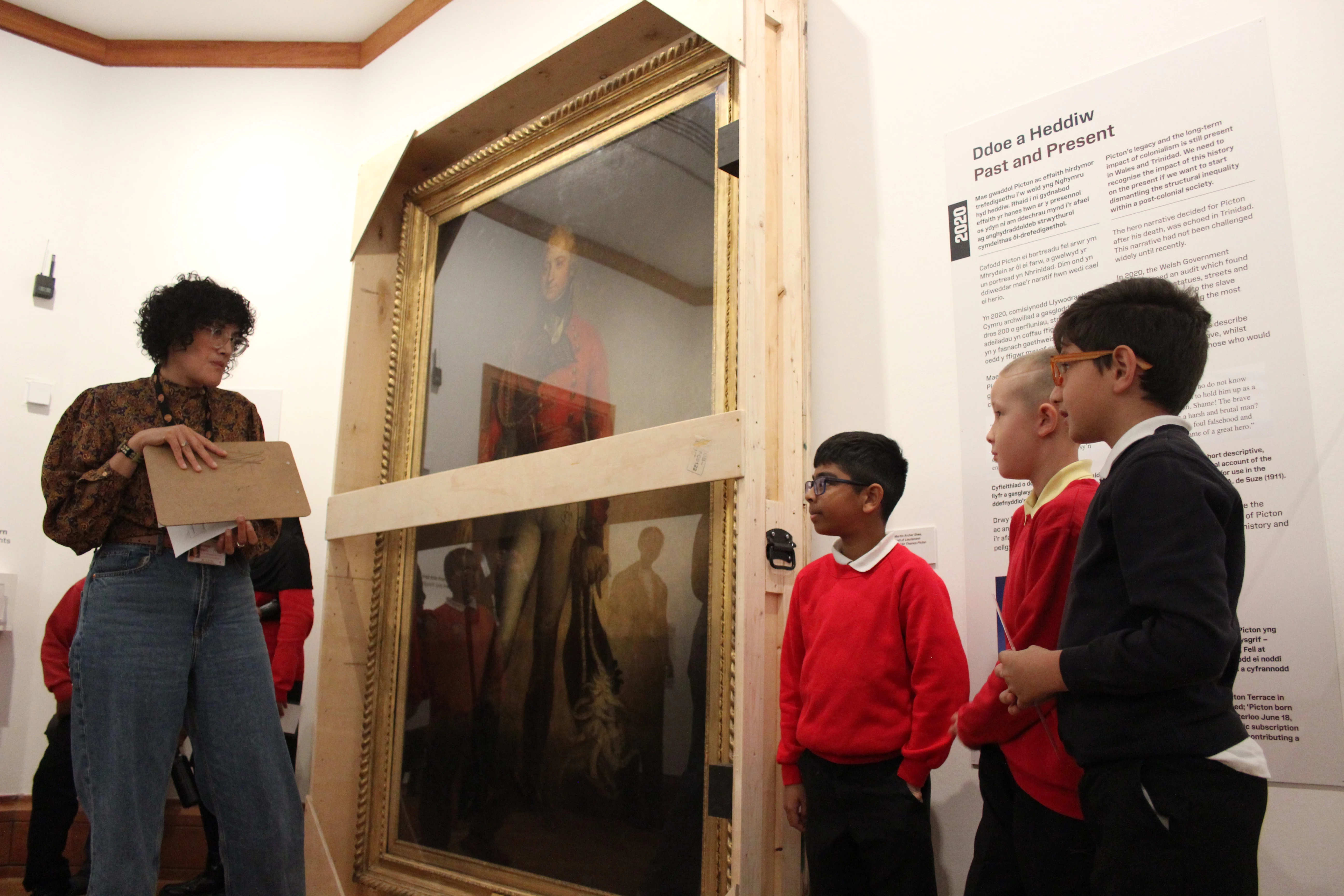 Llun o ddau blentyn ysgol yn trafod arddangosfa Ailfframio Picton gydag aelod o staff