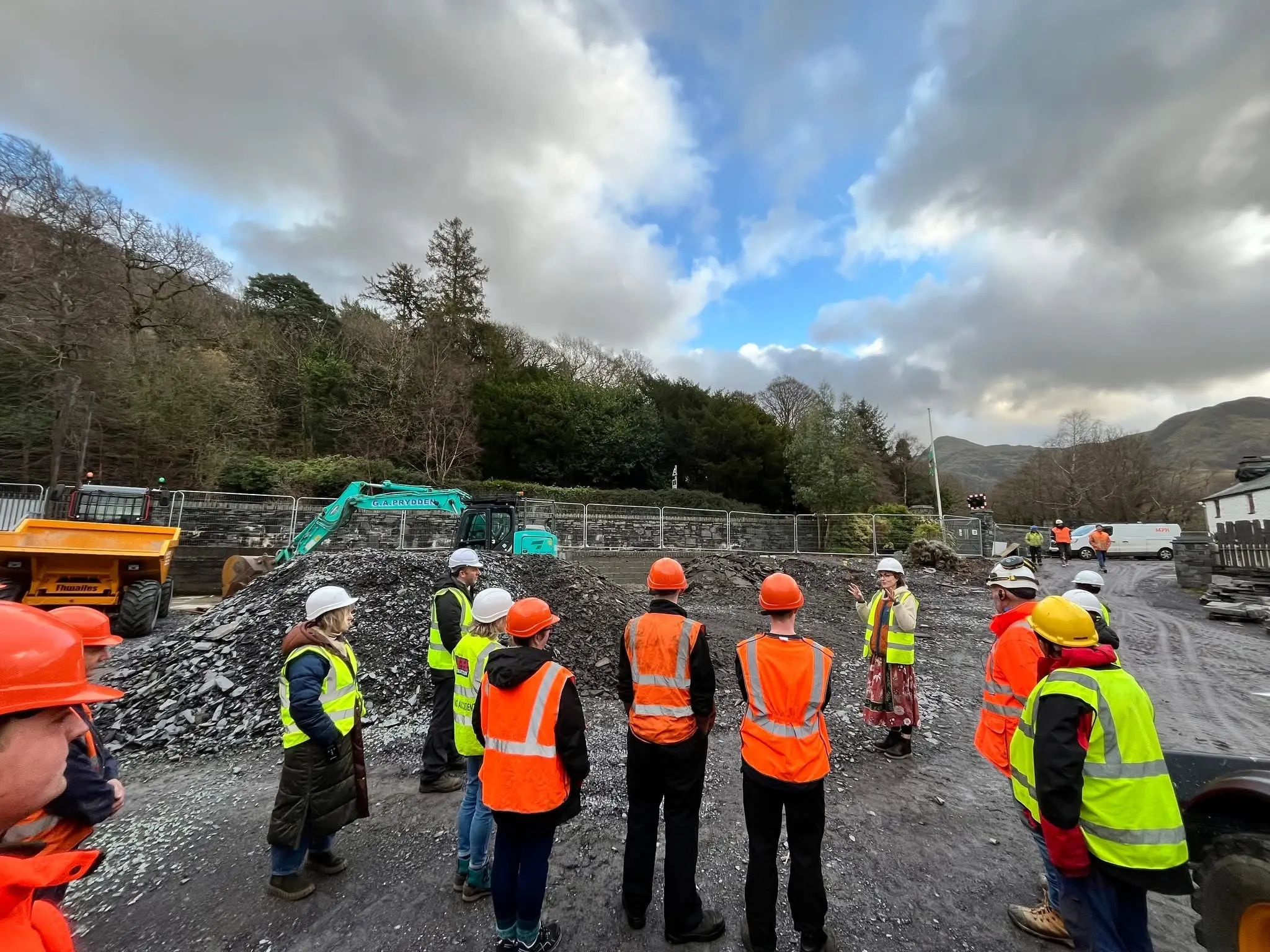 Cri o bobl mewn hetiau caled yn edrych o gwmpas yr ailddatblygiad