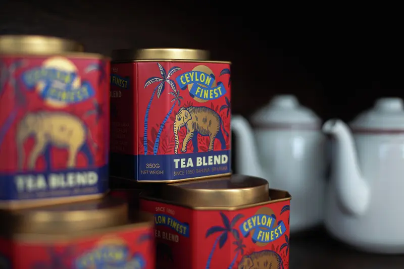 Sawl tun te coch sgwâr gyda chaeadau aur, gyda llun o ddêf drawiadol a'r enw brand Ceylon Finest.